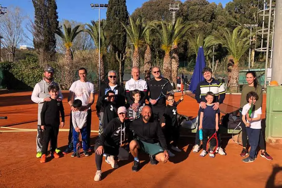 Famiglie con bambini durante attività sportiva di gruppo su campo da tennis all’aperto