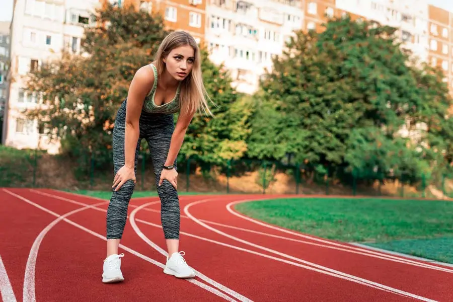 Donna affaticata dopo allenamento su pista mentre riprende a fare sport dopo l’estate